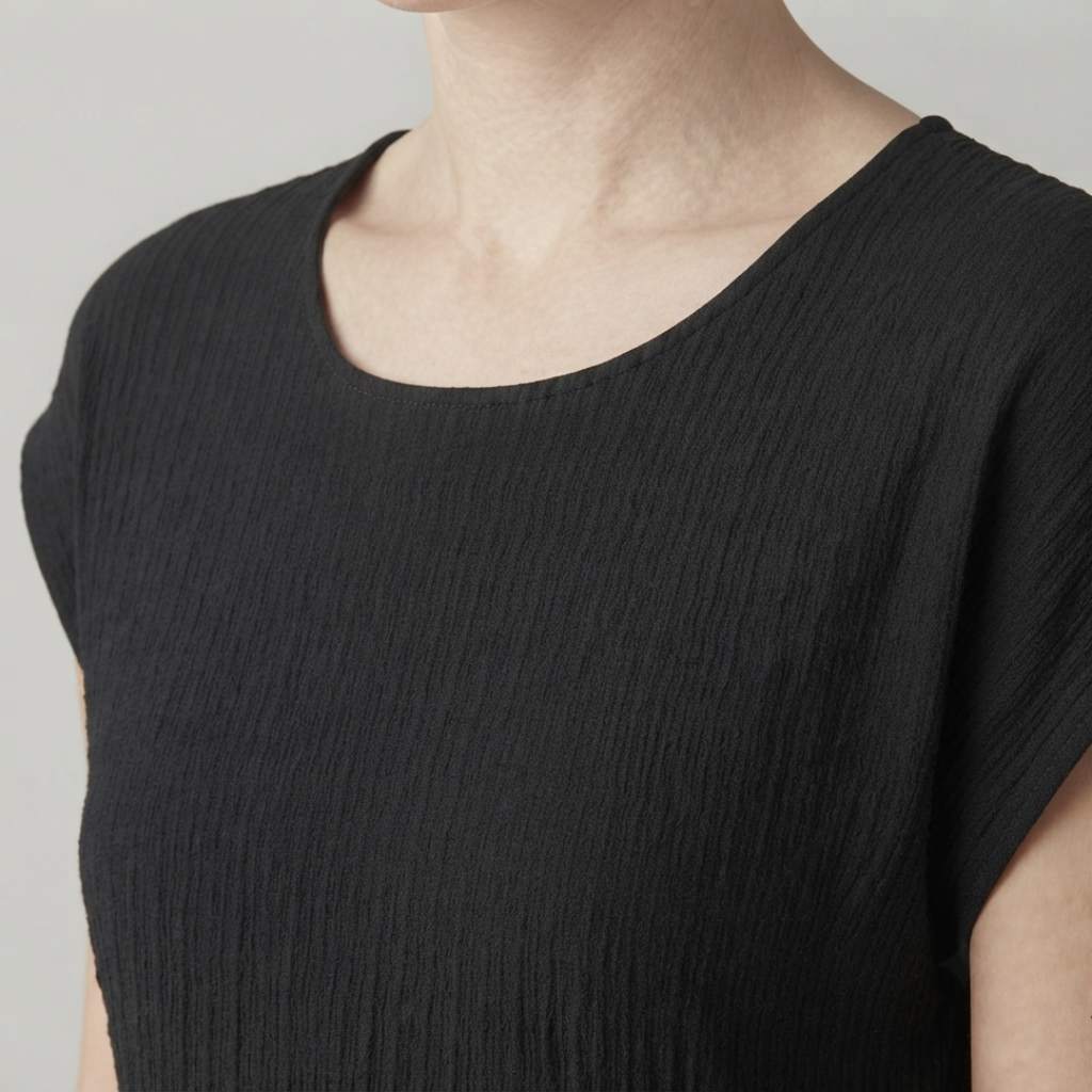Close-up of a person wearing a black short-sleeve top with a textured crinkled fabric and a wide scoop neckline.