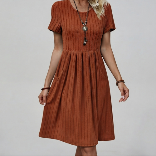 A woman wearing a rust-orange short-sleeve midi dress with a vertical ribbed texture, a gathered waist, and side pockets, photographed against a neutral light gray background.