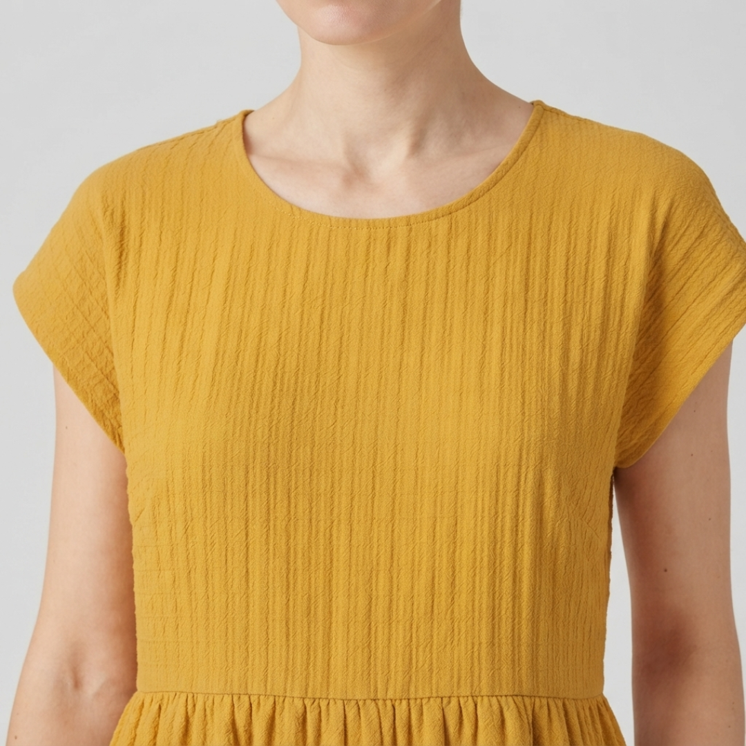 Close-up of a woman wearing a light beige short-sleeve blouse with gathered puff sleeves and a round neckline.