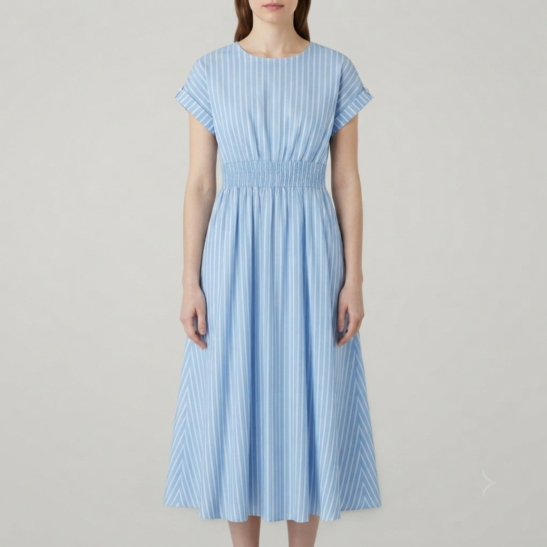 A woman wearing a light blue and white vertically striped midi dress with short sleeves and a smocked waist, photographed against a plain light gray studio background.