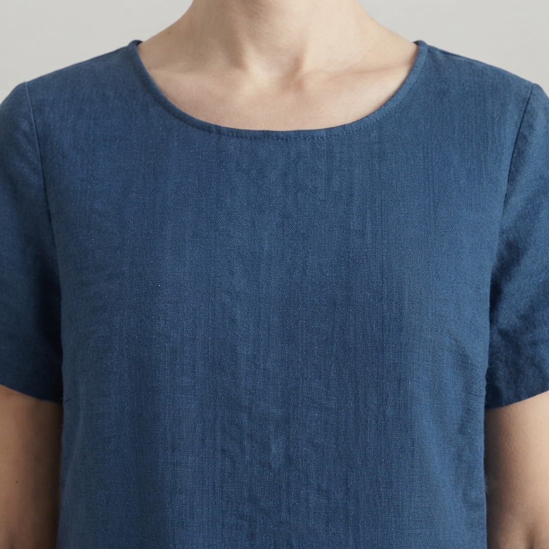 A close-up of a person wearing a short-sleeve blue top with a relaxed, slightly loose fit and a wide, softly curved neckline.