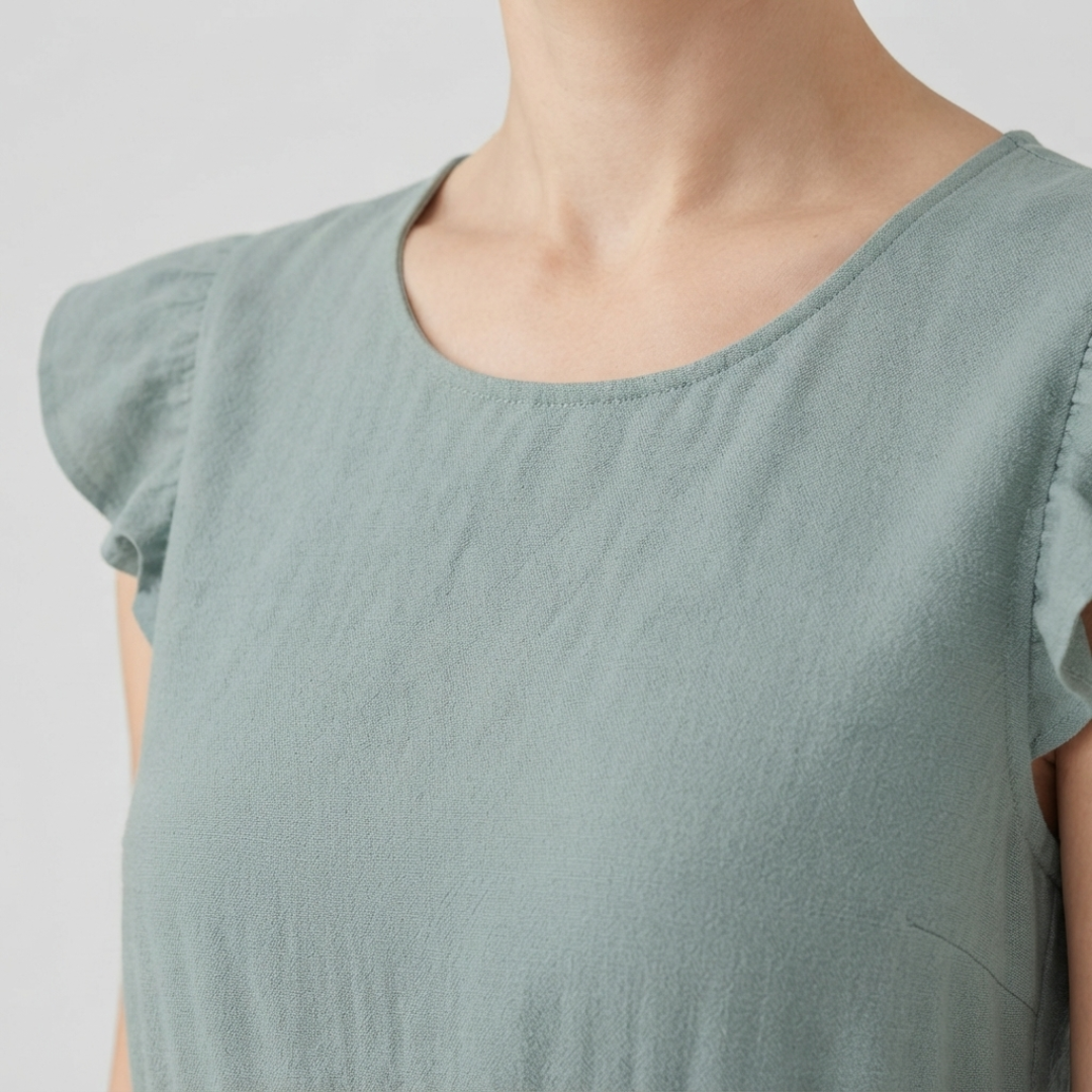 Close-up of a woman wearing a light beige short-sleeve blouse with gathered puff sleeves and a round neckline, shown against a plain light gray background.