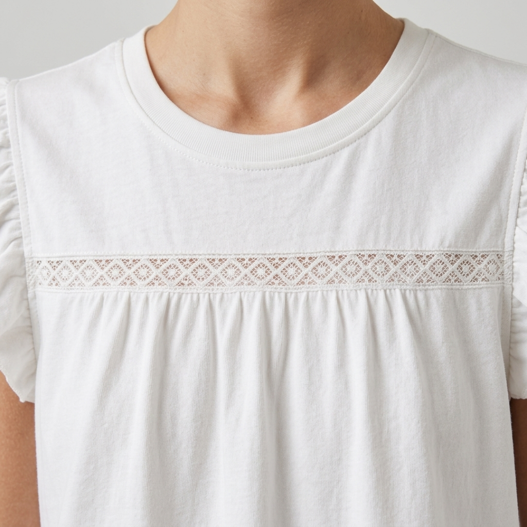 A close-up of a white short-sleeve top worn by a model, featuring a delicate horizontal lace band across the chest and ruffled sleeves.