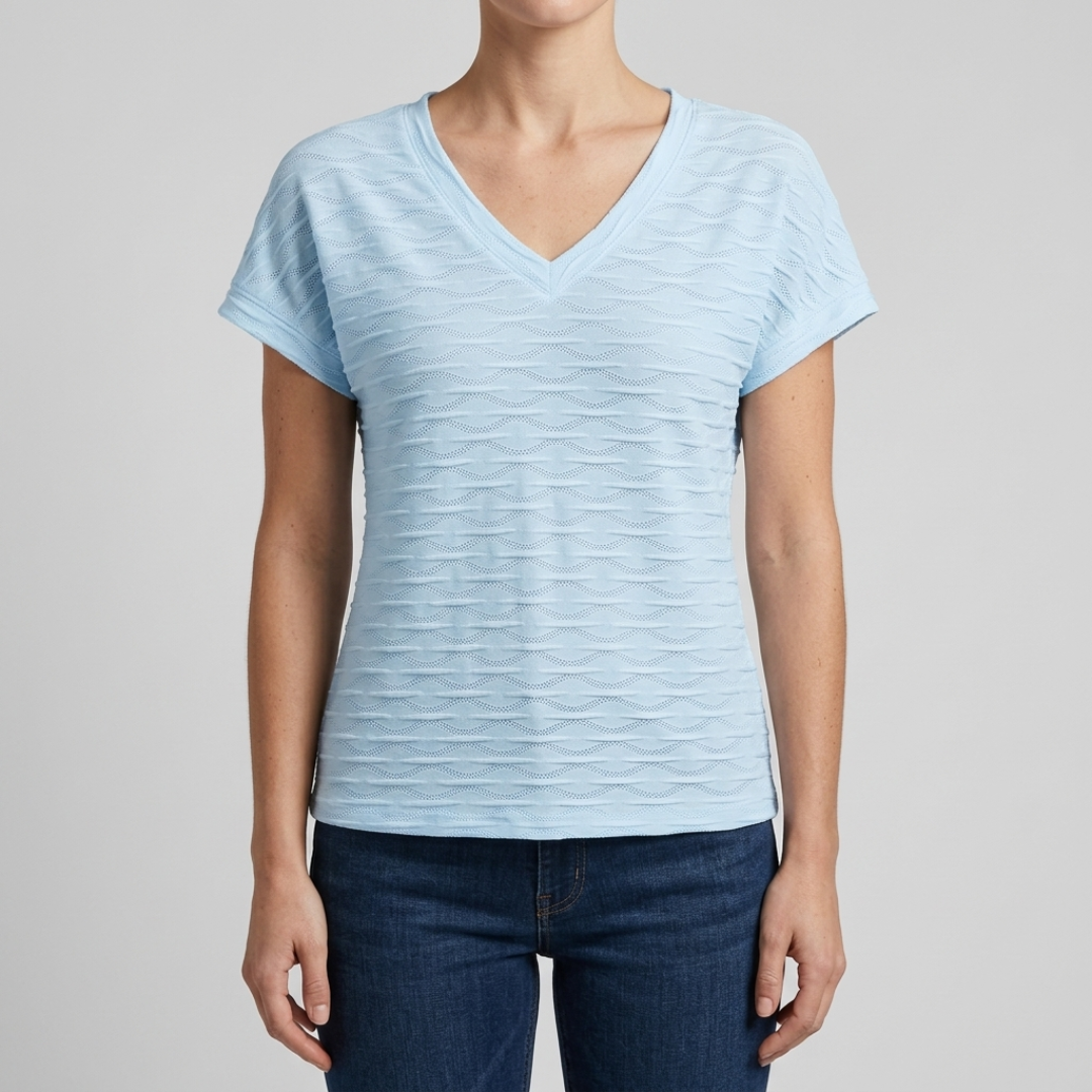 A woman wearing a light blue short-sleeve V-neck t-shirt with a textured, wavy horizontal pattern, paired with dark blue jeans, against a solid light gray background.