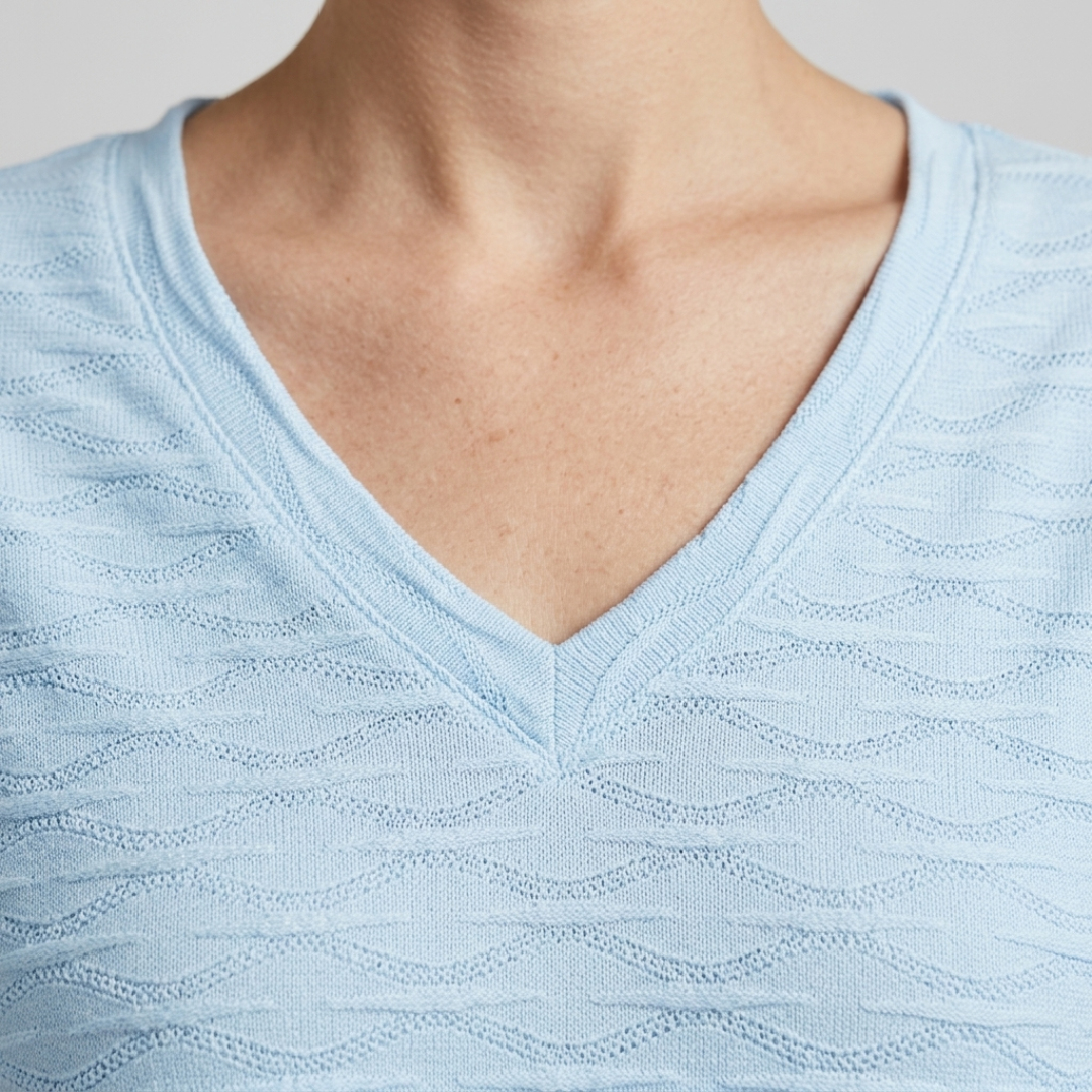 Close-up of a person wearing a light blue textured knit V-neck top, showing the neck and upper chest area.