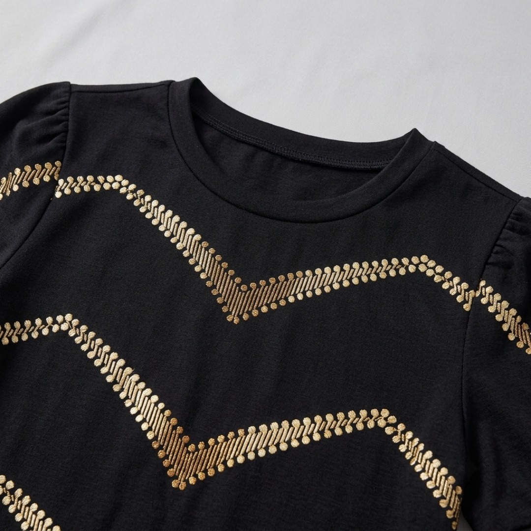A close-up of a black long-sleeve top with gold chevron-patterned sequin embellishments, featuring puffed shoulders and a crew neck.