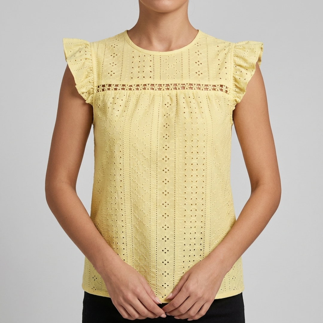 A woman wearing a pale yellow eyelet lace top with ruffled cap sleeves and a decorative horizontal lace band across the chest, shown against a plain light gray studio background.