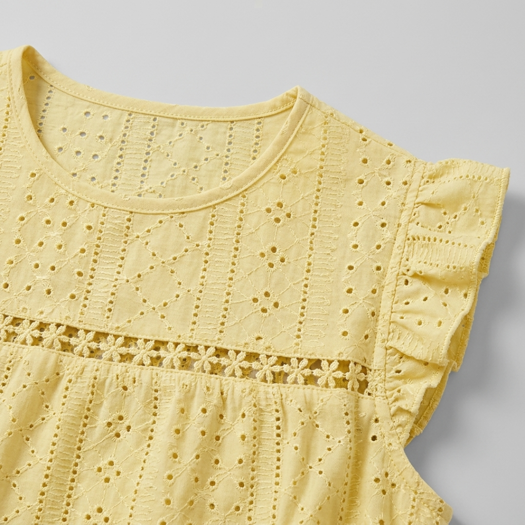 Close-up of a pale yellow eyelet lace top with ruffled sleeves and a floral embroidered band across the chest, shown on a light gray background.