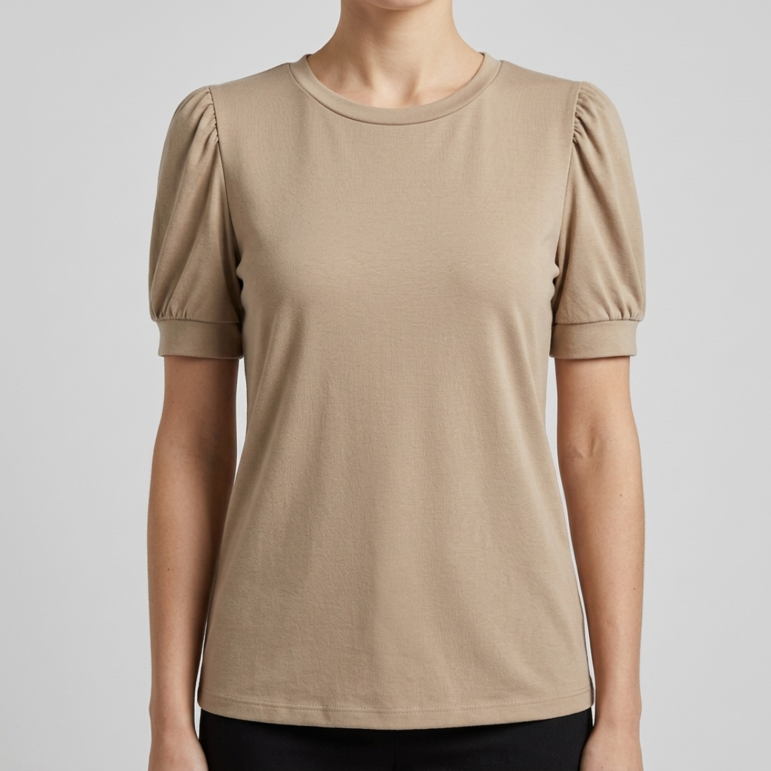 A woman wearing a beige short-sleeve crewneck top with puffed sleeves, shown from the neck down against a light gray studio background.