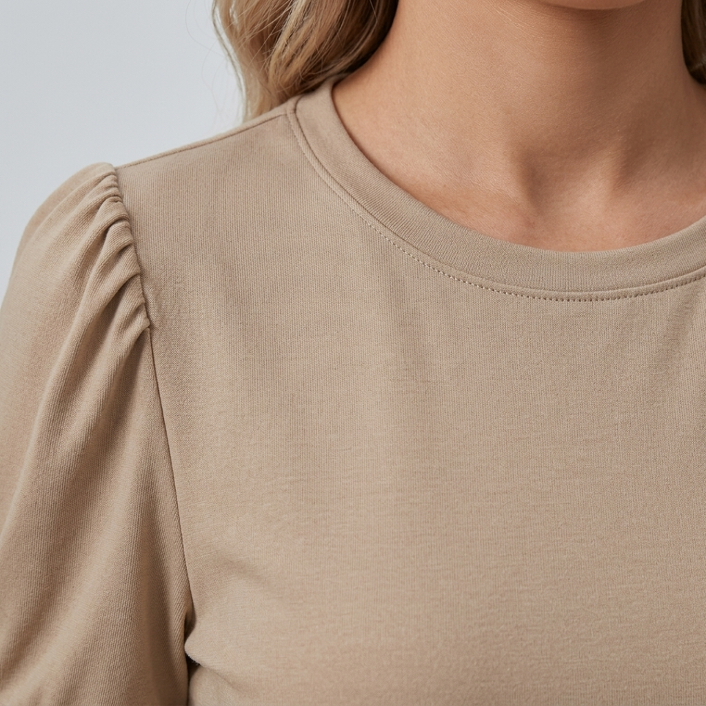 Close-up of a woman wearing a beige long-sleeve top with gathered puff sleeves and a crew neckline.